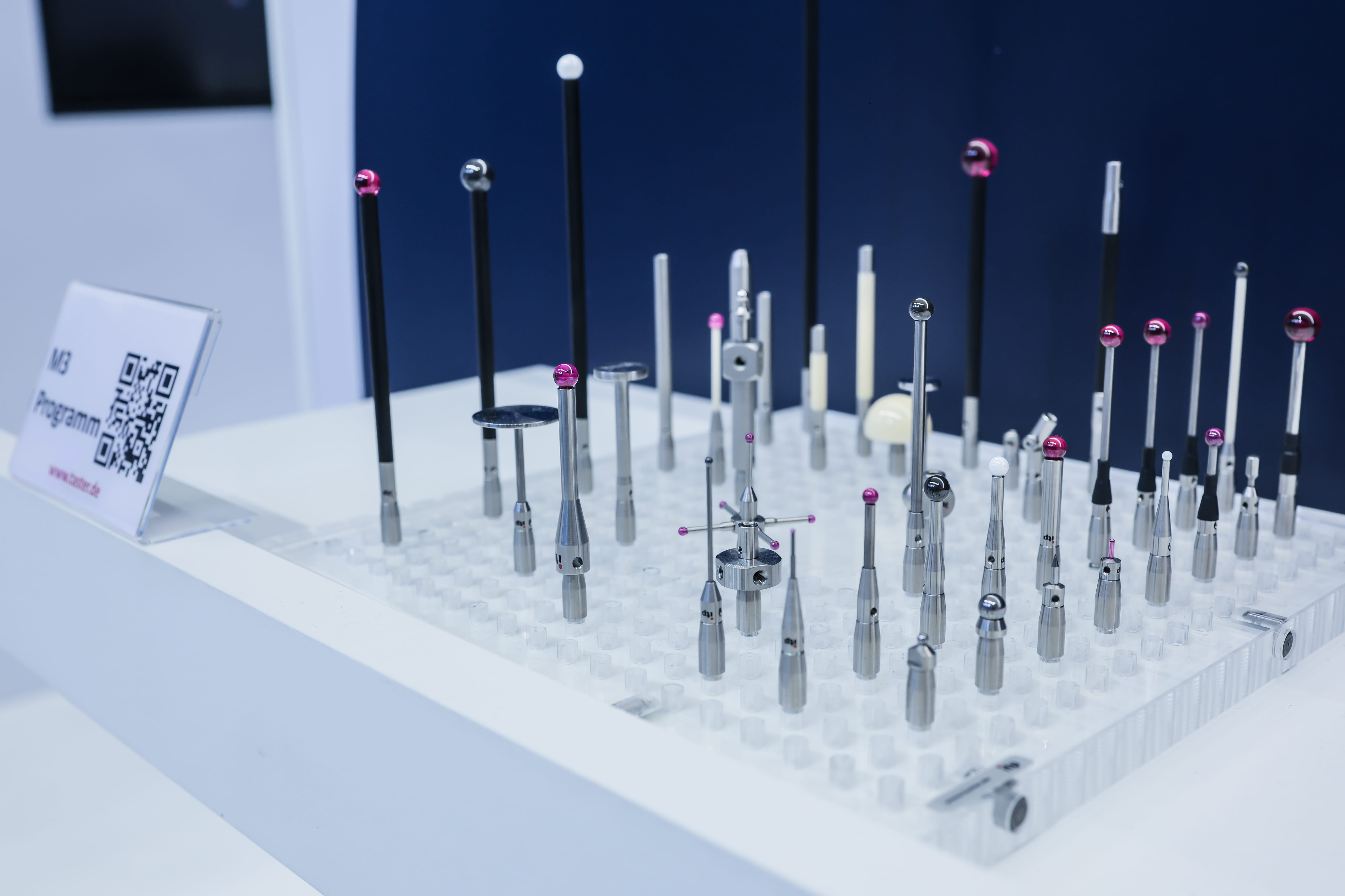 Assorted metrology styli stand on a clear display tray. Ruby, ceramic, and metal tips show varied probe shapes.