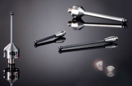 Four diamond styli in varied lengths and angles rest on a glossy black surface. Reflections and loose diamonds add shine.
