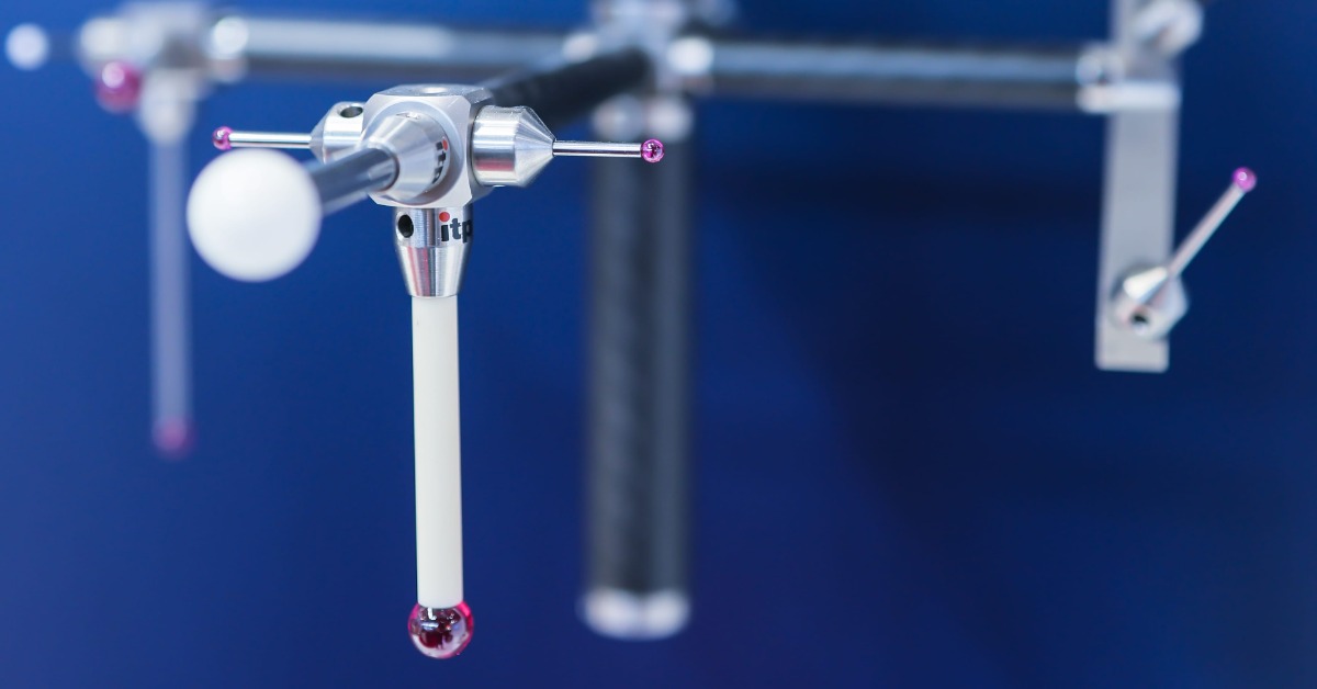 A multi-tip probe assembly hangs below a CMM head. Ruby tips and a white sphere extend from the fixture.