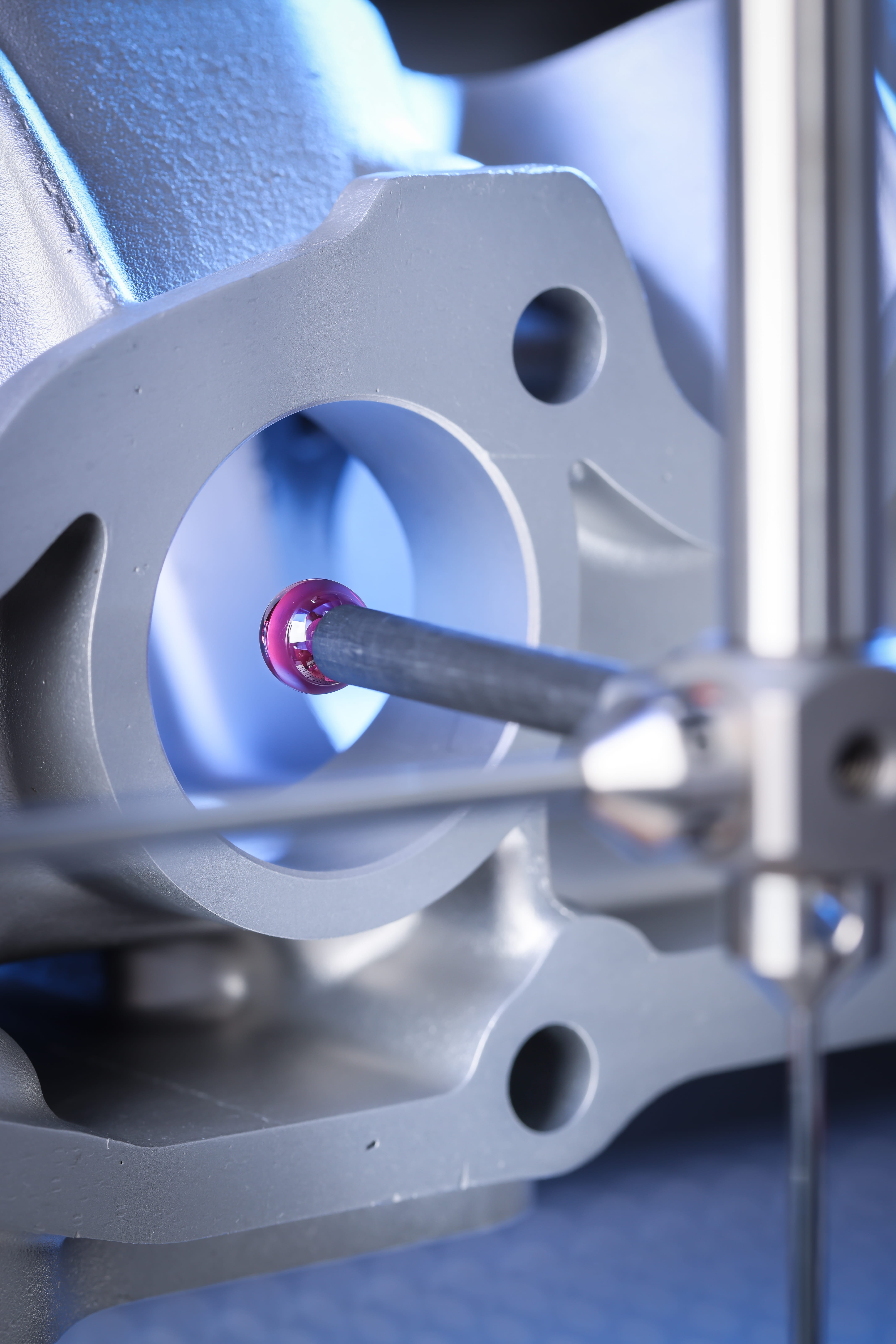A red spherical probe interacting with the inner edge of a machined part with circular holes and blue lighting.