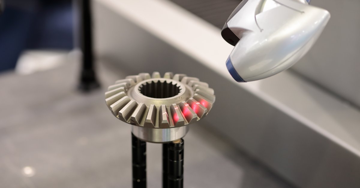 A CMM machine uses lasers to take an accurate measurement of a metal part. The part has a red glow where the laser is pointed.