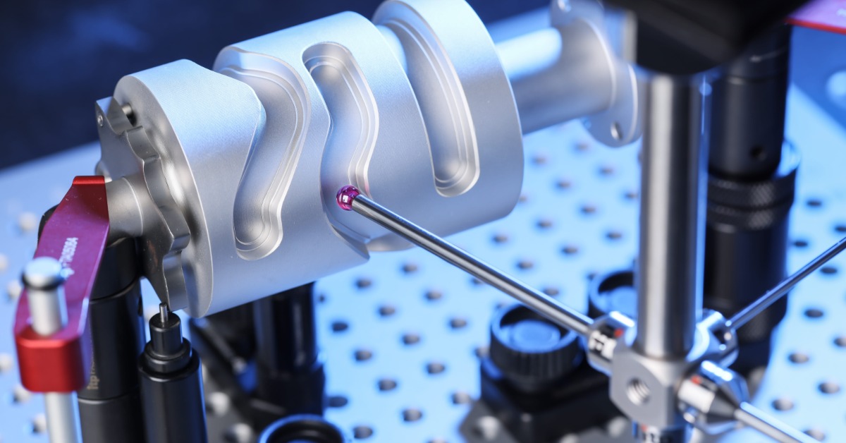 A red spherical probe touching a machined silver cylinder held on a perforated blue inspection table.
