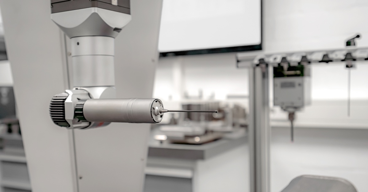 A coordinate measuring machine with a long stylus on attachment. More equipment is in the background.