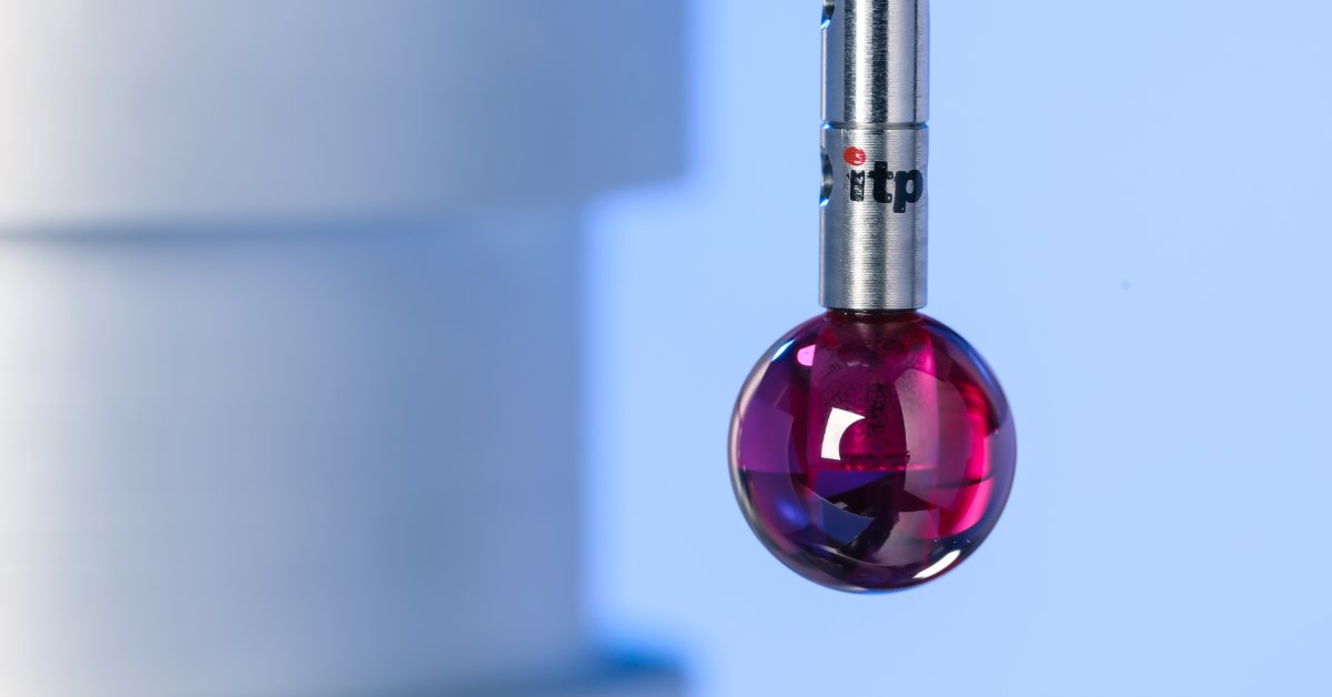 A shiny red probe tip hanging from a vertical metal tool beside a pale blue object against a soft blue background.