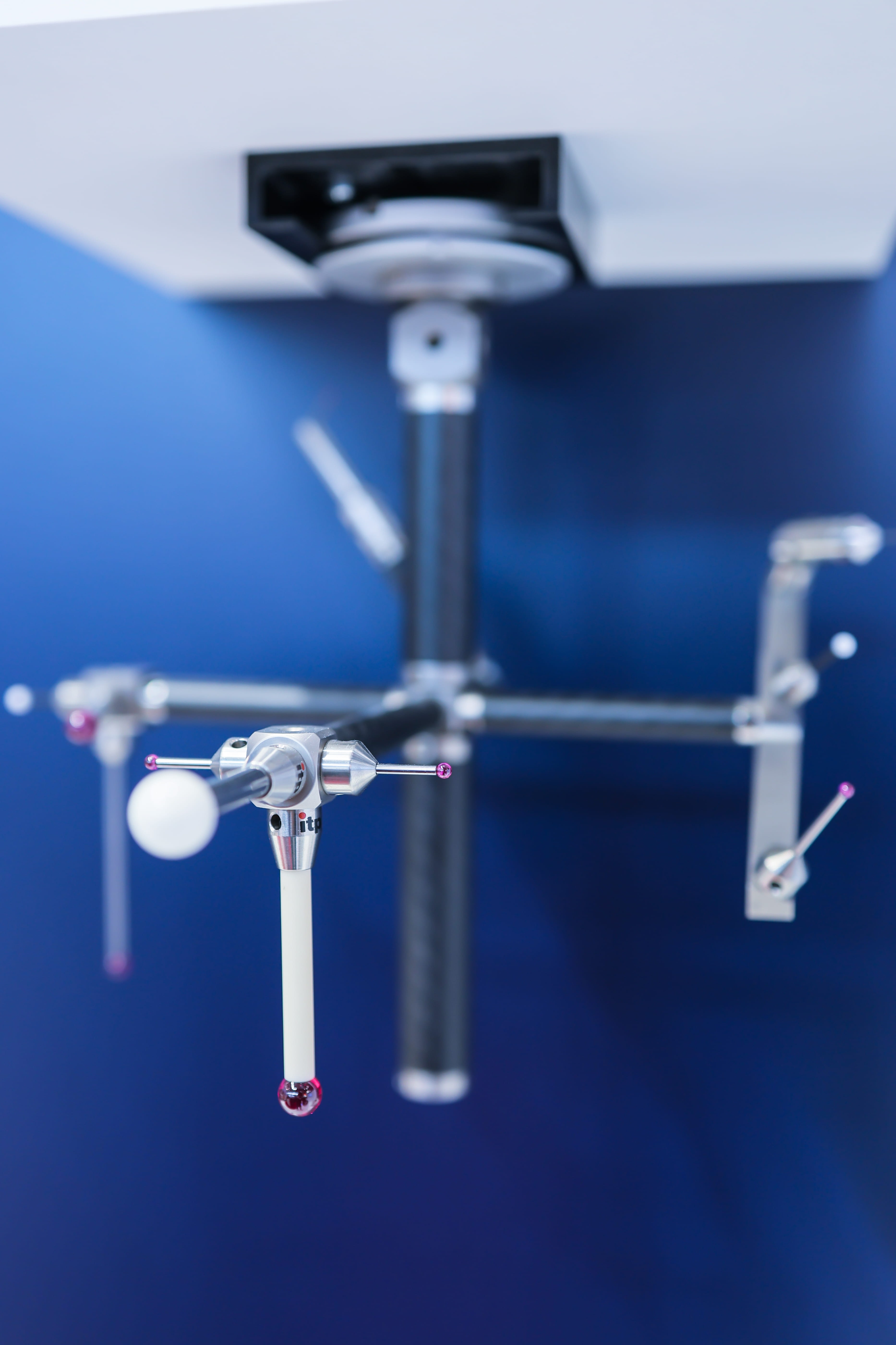 A multi-tip probe assembly with red and white spheres hanging against a dark blue background with blurred arms.