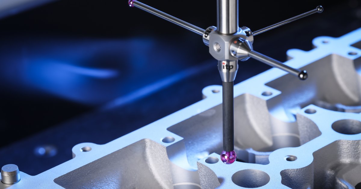 A shiny red probe tip positioned above machined white parts on a metal inspection table with blue light behind.