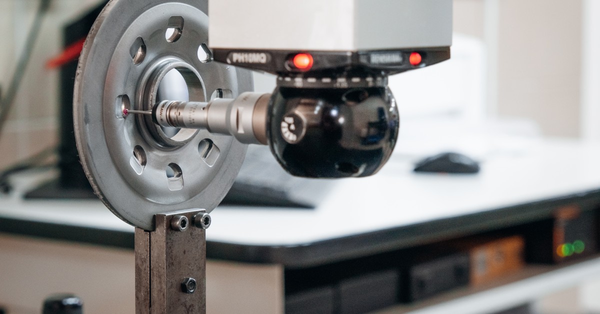 A coordinate measuring machine is working to measure a metal disk. The stylus attached to the machine is touching the metal.