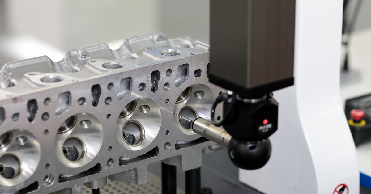 A coordinate measuring machine taking measurements of a metal part with lots of grooves and holes.