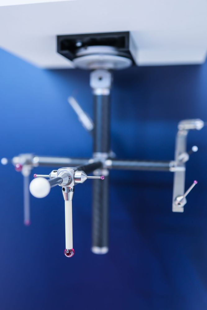 A multi-tip probe assembly with red and white spheres hanging against a dark blue background with blurred arms.
